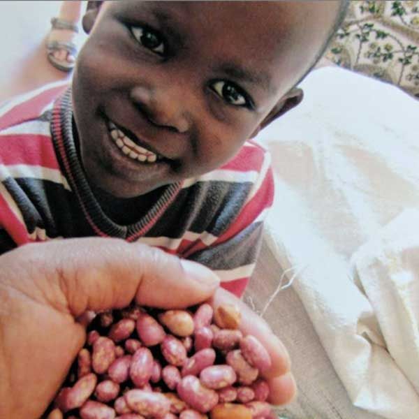 Young boy smiling behind a cupped handful of speckled beans held up to the camera.