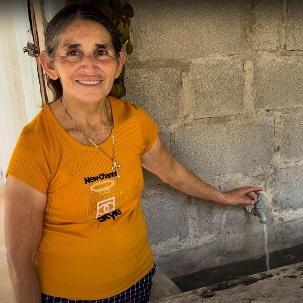Woman standing beside a wall with clean water flowing from a spigot in Honduras.