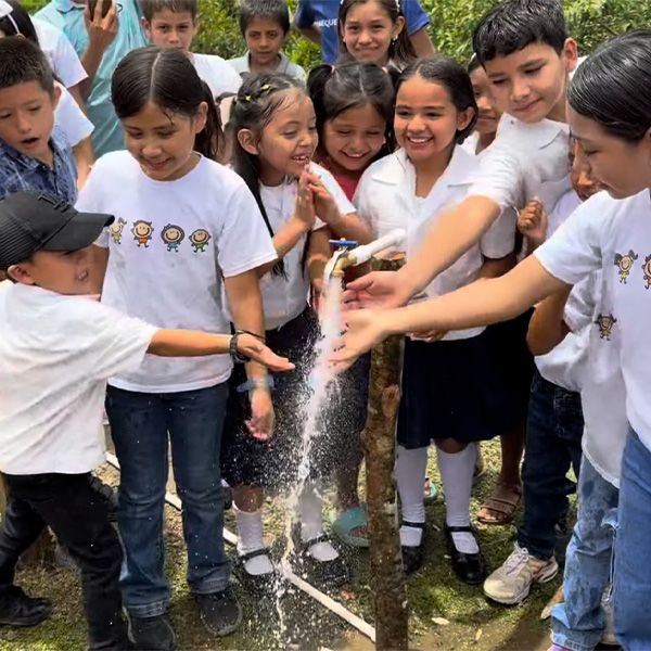 Schoolchildren crowding around a newly installed tap, reaching out together to catch the water pouring from it.